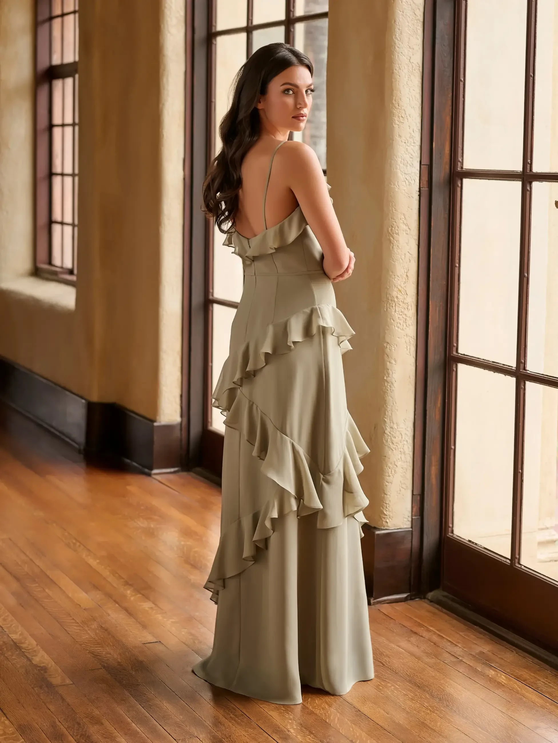 Model is wearing a Christina Wu Celebration 22250, a sage green v-neck spaghetti strap chiffon A-line with asymmetrical ruffles on the bodice and skirt.