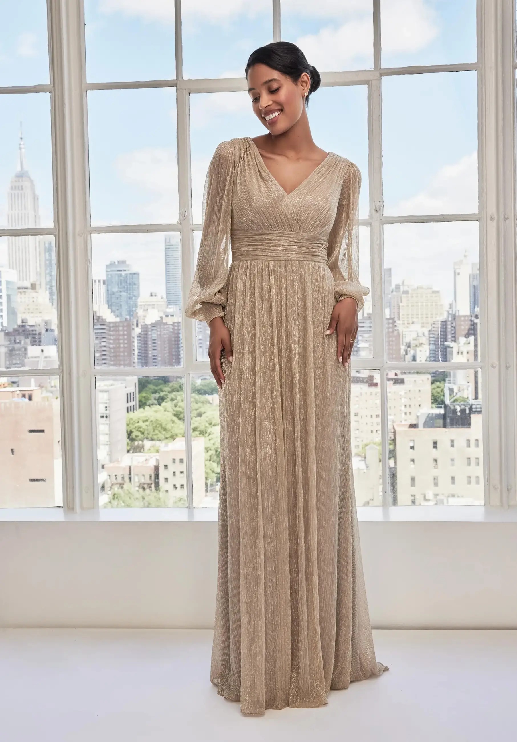 Model is wearing an A-line dress with sheer bishop sleeves and metallic fabric
