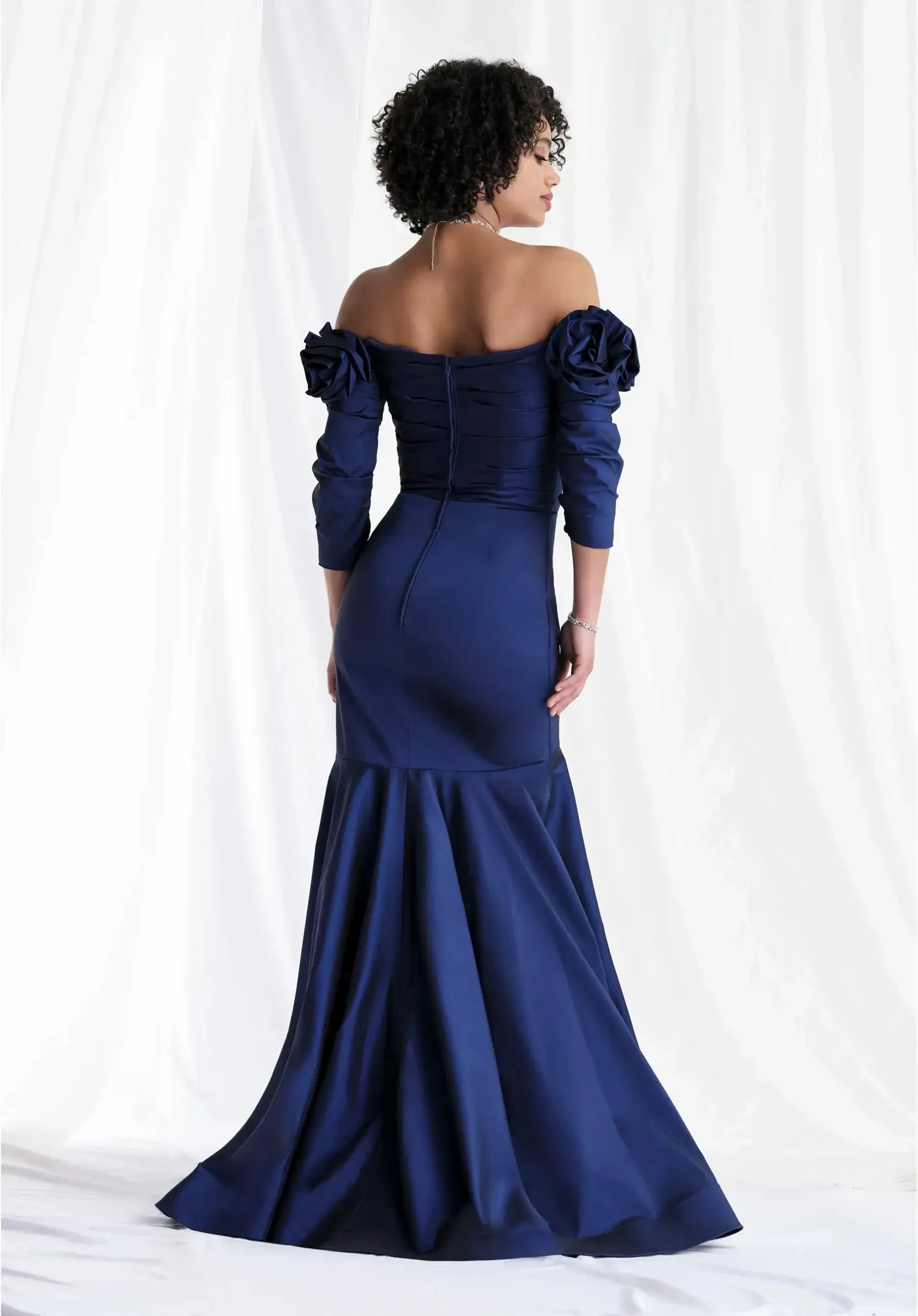 Off-the-shoulder stretch taffeta mermaid gown with draped details, 3/4 sleeves, and a rosette accent at the waist.