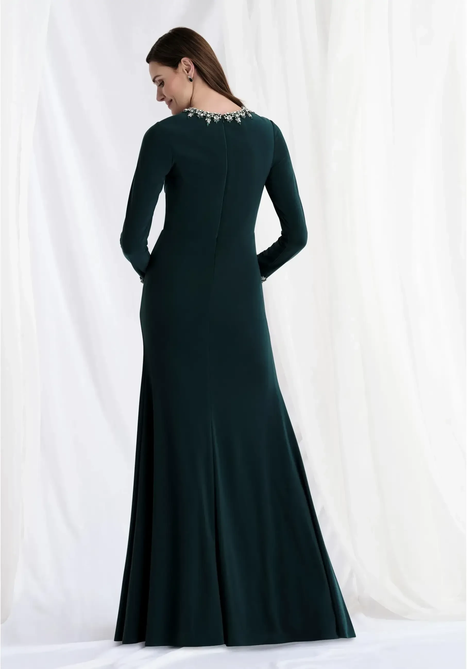 Jersey sheath gown with an asymmetrical drape, beaded jewel neckline, and long beaded sleeves.