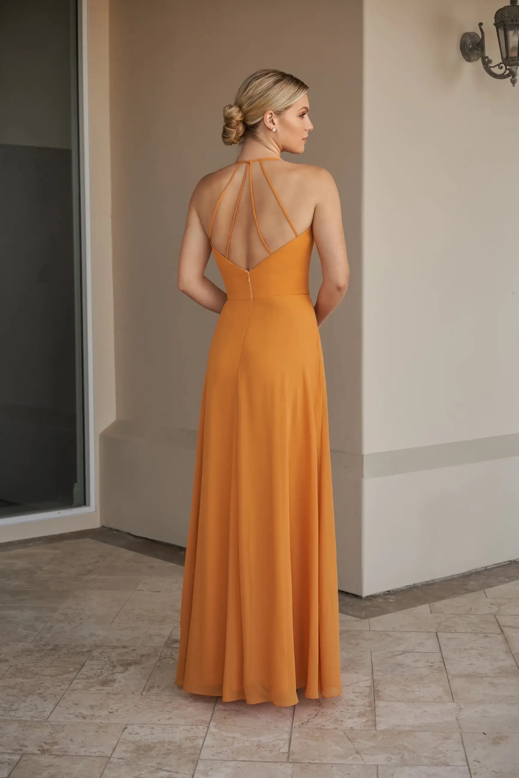 Model is wearing a flowy chiffon bridesmaid dress with a cowl neckline and halter back