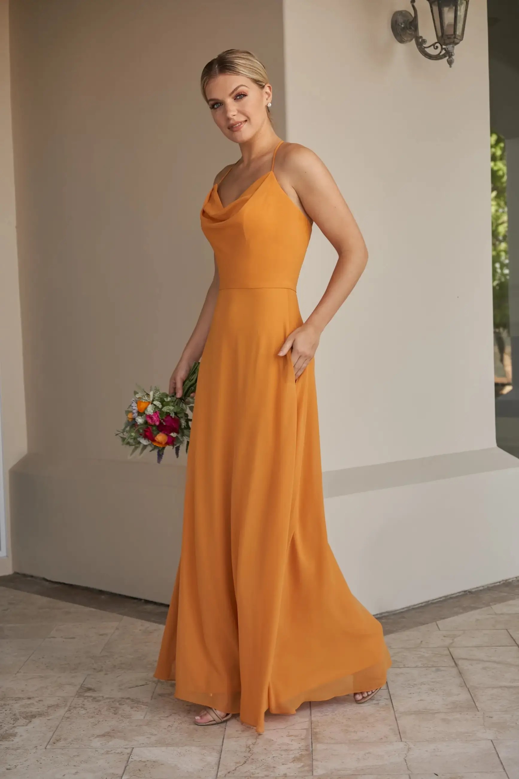 Model is wearing a flowy chiffon bridesmaid dress with a cowl neckline and halter back