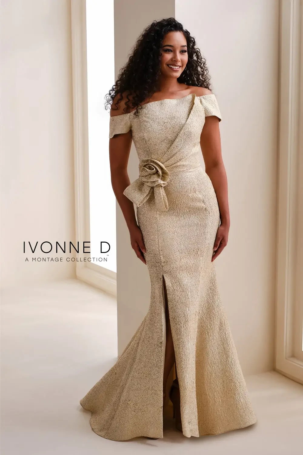 A woman in a gold off-the-shoulder dress with a fitted silhouette and a decorative bow at the waist, standing confidently against a light-colored background.