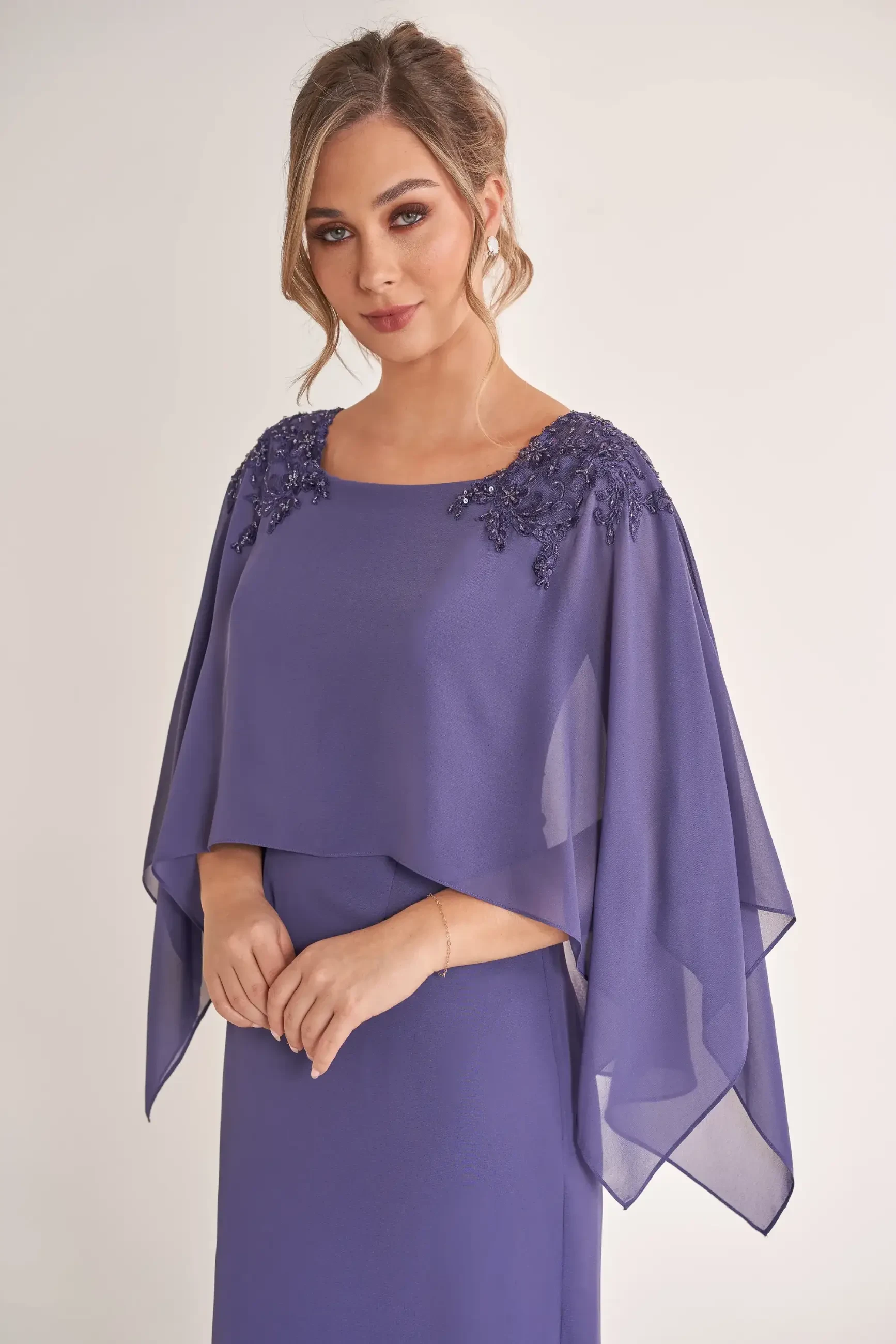 Woman in an elegant purple dress with sheer cape sleeves and intricate beading on the shoulders, exuding a graceful and confident demeanor.