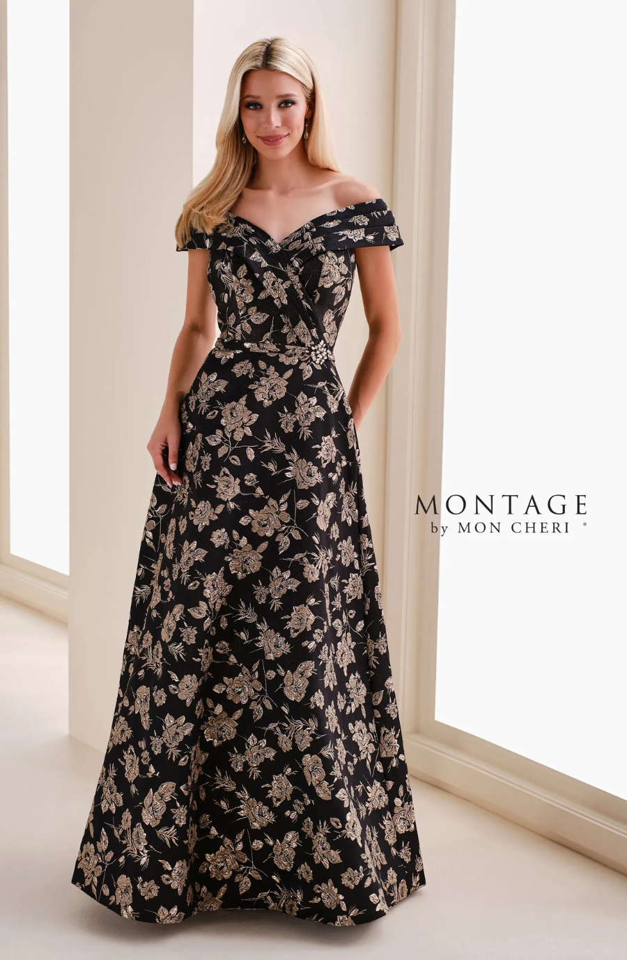 A woman wearing an off-the-shoulder, floral evening gown standing in a well-lit room.